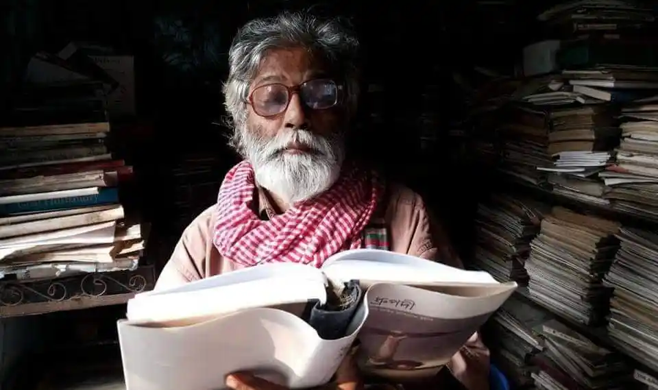 বই পড়ছেন একজন বৃদ্ধ ব্যক্তি, পেছনে বইয়ের স্তূপ।. Channel i News - চ্যানেল আই নিউজ