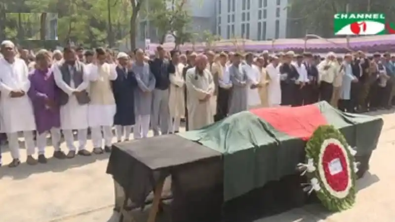 Bangladeshi people gather for funeral prayer around a coffin draped with the national flag. Channel i News - চ্যানেল আই নিউজ