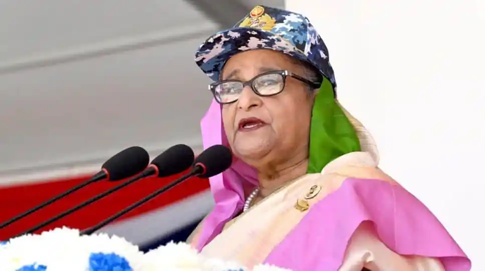প্রধানমন্ত্রী শেখ হাসিনা ভাষণ দিচ্ছেন, পেছনে মাইক্রোফোন ও ব্যানার. Channel i News - চ্যানেল আই নিউজ