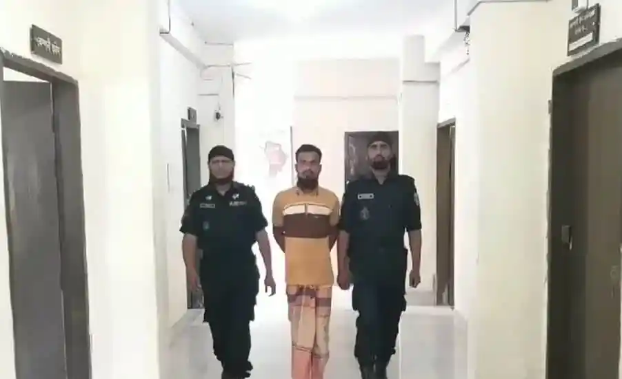 আদালত কক্ষে একজন আসামি, দুই পুলিশ কর্মকর্তা তার পাশে।. Channel i News - চ্যানেল আই নিউজ