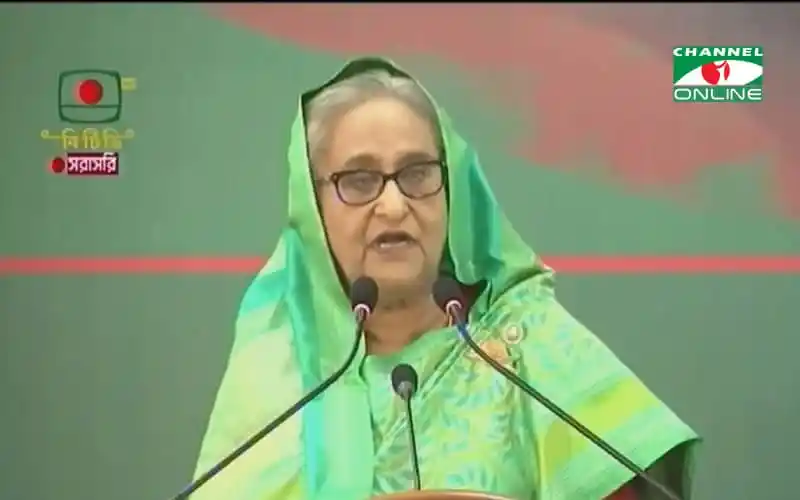 প্রধানমন্ত্রী ভাষণ দিচ্ছেন, সবুজ শাড়ি পরা, পেছনে টেলিভিশন স্ক্রিন।. Channel i News - চ্যানেল আই নিউজ