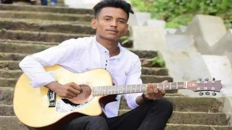 Young man playing guitar outdoors in a natural setting. Channel i News - চ্যানেল আই নিউজ
