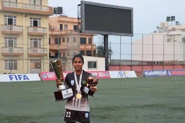 ফুটবল মাঠে চ্যাম্পিয়ন গোলরক্ষক ট্রফি ও মেডেল নিয়ে হাসছেন. Channel i News - চ্যানেল আই নিউজ