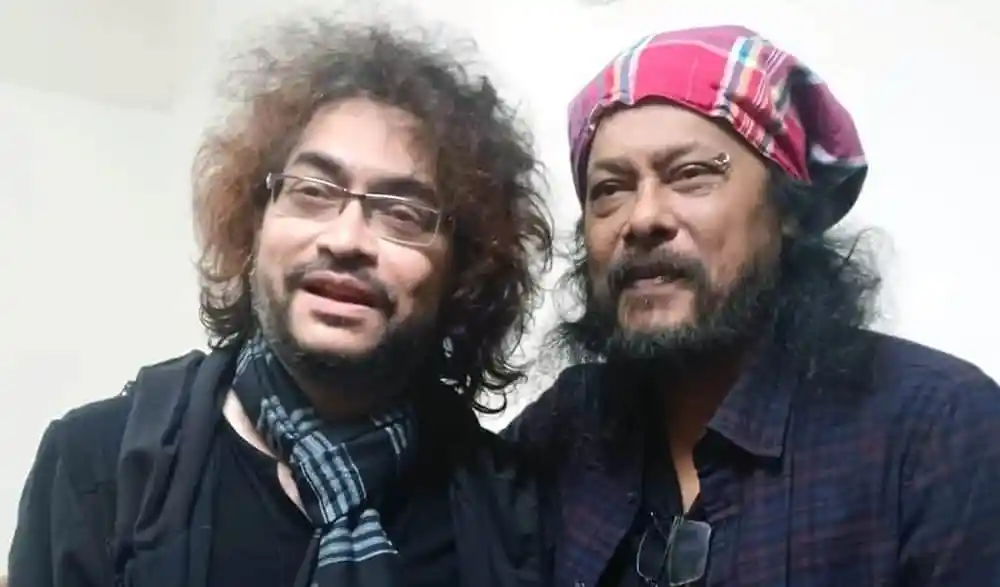 দুই ব্যক্তি হাসিমুখে, একজনের মাথায় পাগড়ি, অন্যজনের চুল কুঁচকানো. Channel i News - চ্যানেল আই নিউজ