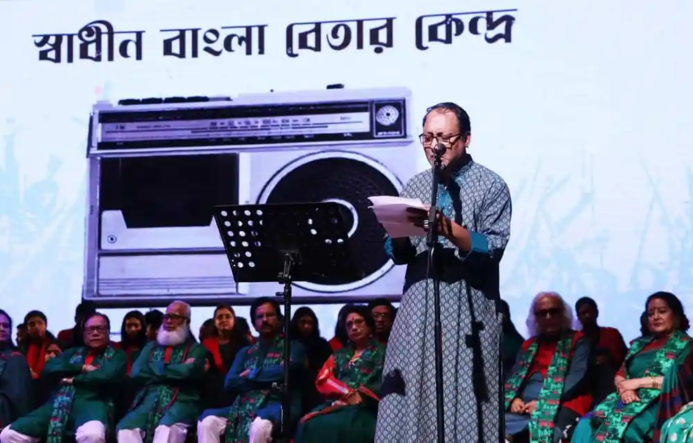 শ্রোতাদের সামনে কবিতা পাঠ করছেন একজন কবি, পেছনে বড় অডিও সিস্টেম দেখা যাচ্ছে. Channel i News - চ্যানেল আই নিউজ