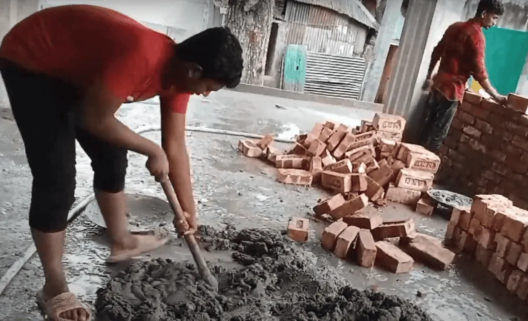 ছেলে একজন রিজার্ভার দিয়ে ইটের কাজ করছে, নির্মাণাধীন ভবনের পাশে।. Channel i News - চ্যানেল আই নিউজ