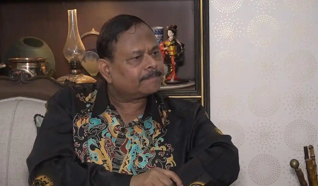 বাংলাদেশি ব্যক্তি বসে আছেন, পটভূমিতে আসবাবপত্র ও সজ্জা দেখা যাচ্ছে. Channel i News - চ্যানেল আই নিউজ
