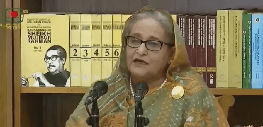 প্রধান অতিথি বক্তৃতা দিচ্ছেন, পুস্তকশালা ও বইয়ের সংগ্রহের পেছনে বইয়ের শেলফ. Channel i News - চ্যানেল আই নিউজ