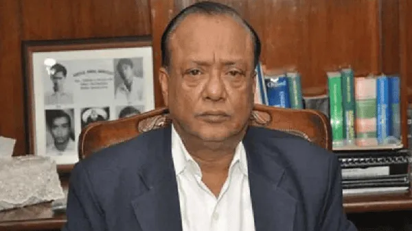 আব্দুল আউয়াল মিন্টু বসে আছেন, পেছনে বইয়ের তাক ও ছবি ফ্রেম দেখা যাচ্ছে. Channel i News - চ্যানেল আই নিউজ