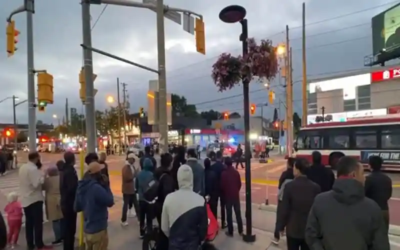 People gather at a busy street corner in Canada during evening hours. Channel i News - চ্যানেল আই নিউজ