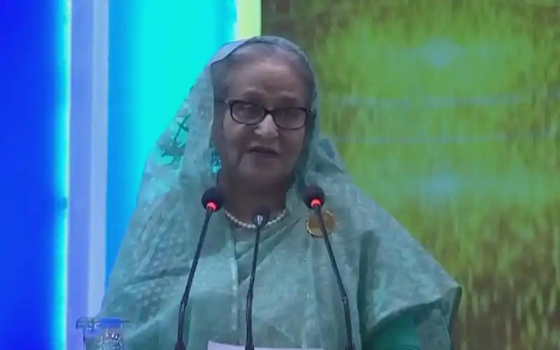 প্রধানমন্ত্রী ভাষণ দিচ্ছেন, পটভূমিতে সবুজ ও নীল রঙের ব্যাকড্রপ. Channel i News - চ্যানেল আই নিউজ