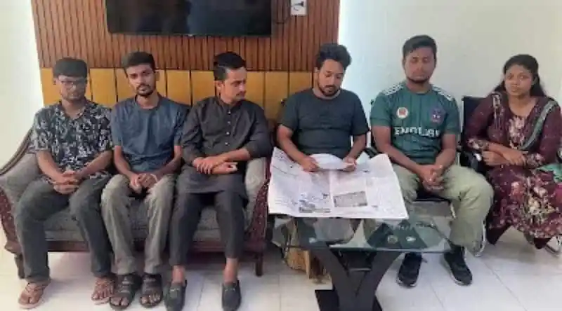 ছয়জন সমন্বয়ক বসে সংবাদপত্র পড়ছেন, একটি টিভি স্ক্রিন পেছনে দেখা যাচ্ছে. Channel i News - চ্যানেল আই নিউজ