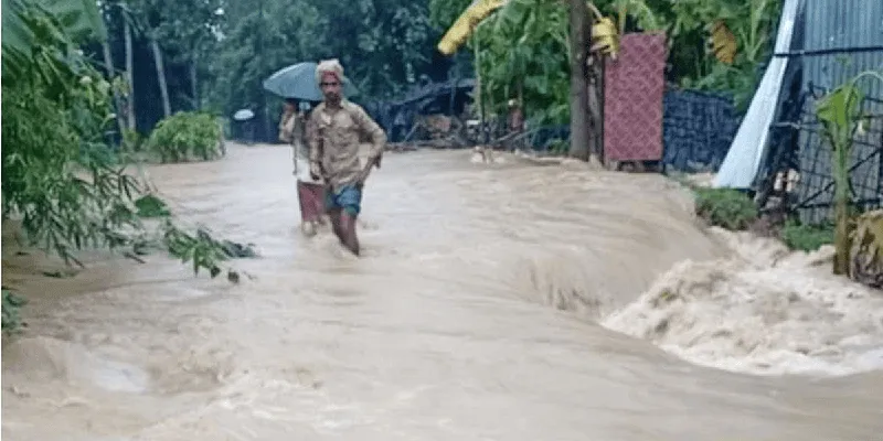 বন্যার পানিতে রামুর দুই যুবক হাঁটছেন, চারপাশে জলাবদ্ধতা দেখা যাচ্ছে. Channel i News - চ্যানেল আই নিউজ