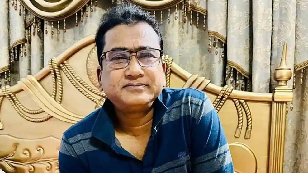বাংলাদেশের একজন রাজনীতিবিদ বসে আছেন, পটভূমিতে সিল্কের পর্দা ও আসবাব।. Channel i News - চ্যানেল আই নিউজ