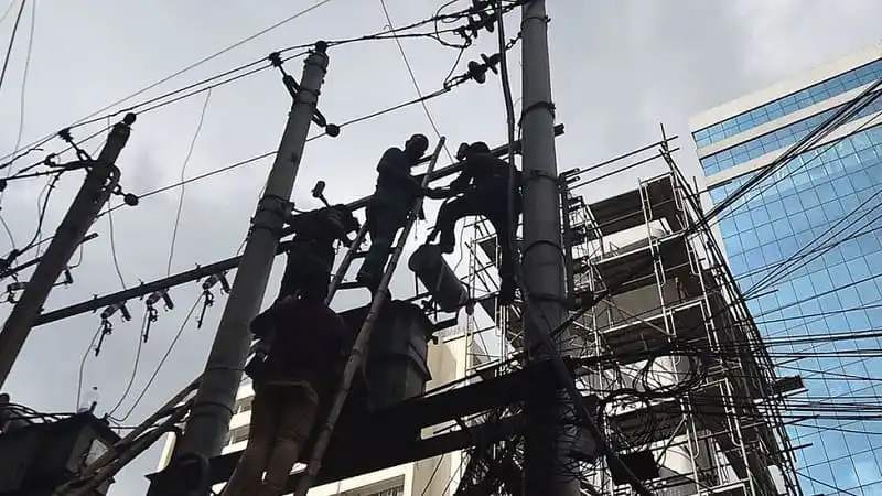 শ্রমিকরা বিদ্যুৎ লাইনে কাজ করছে, উচ্চ ভবনের পাশে. Channel i News - চ্যানেল আই নিউজ
