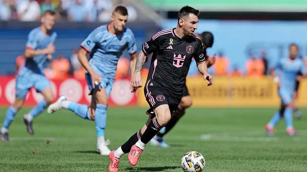 Football player in black jersey dribbling ball during match with opponents in blue jerseys. Channel i News - চ্যানেল আই নিউজ