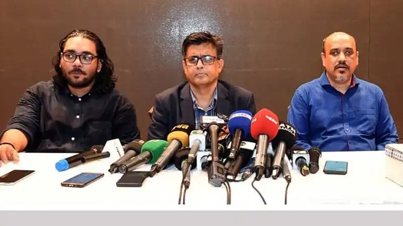 সংবাদ সম্মেলনে তিনজন বক্তা microphones ও মোবাইলের সামনে বসে আছেন. Channel i News - চ্যানেল আই নিউজ