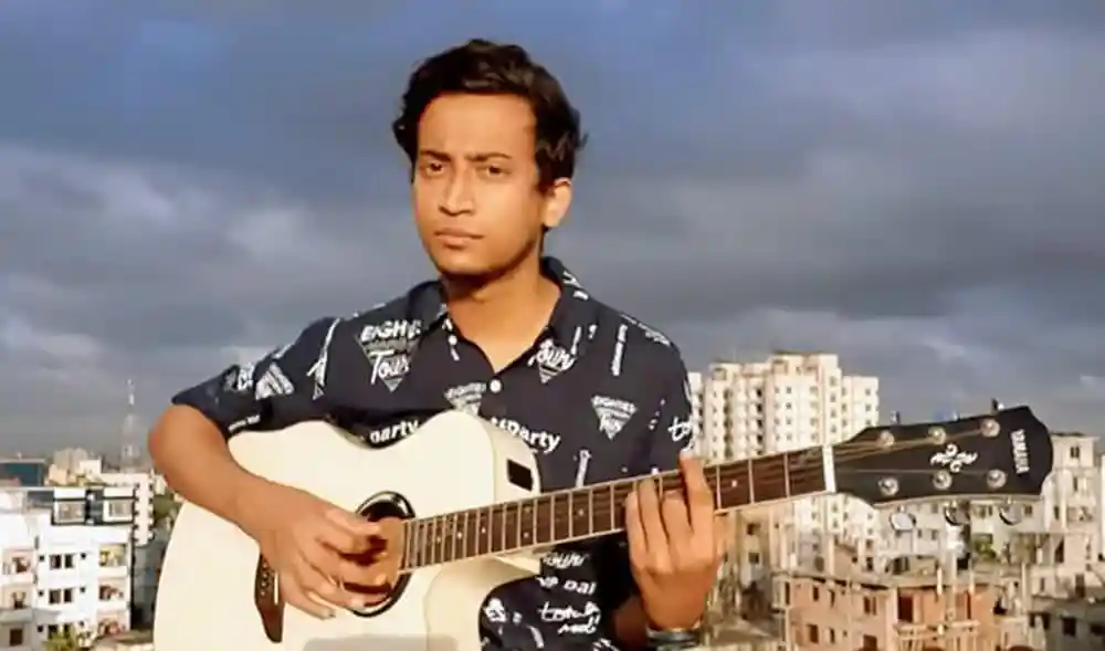 তাসরিফ গিটার বাজাচ্ছেন, শহরের পটভূমিতে আকাশ মেঘাচ্ছন্ন. Channel i News - চ্যানেল আই নিউজ