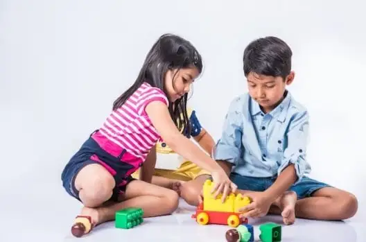 দুটি শিশু খেলনা দিয়ে খেলছে, একে অপরের পাশে বসে।. Channel i News - চ্যানেল আই নিউজ