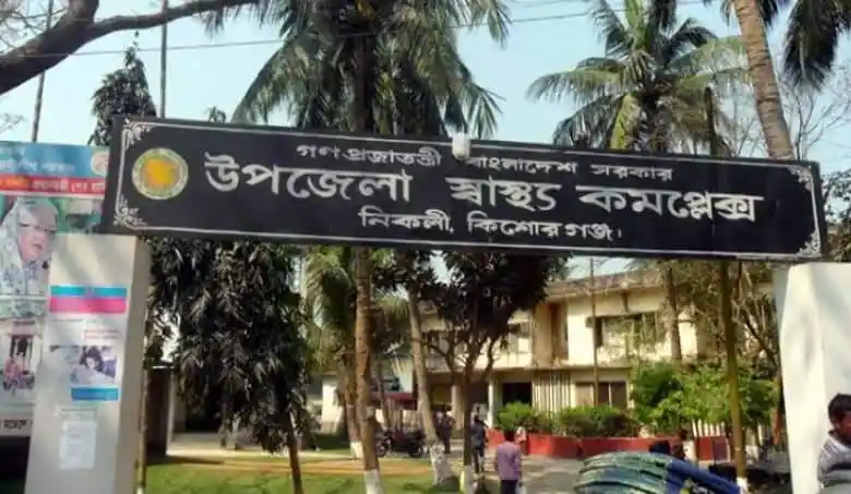 উপজেলা স্বাস্থ্য কমপ্লেক্সের প্রবেশদ্বার, গেটের উপর বাংলা লেখা. Channel i News - চ্যানেল আই নিউজ