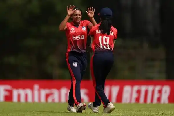 Two female cricket players celebrating on the field in red uniforms. Channel i News - চ্যানেল আই নিউজ