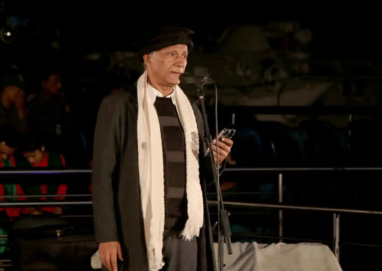 বয়সী নারী বক্তা মঞ্চে বক্তৃতা দিচ্ছেন, পেছনে যুদ্ধজাহাজ দেখা যাচ্ছে. Channel i News - চ্যানেল আই নিউজ