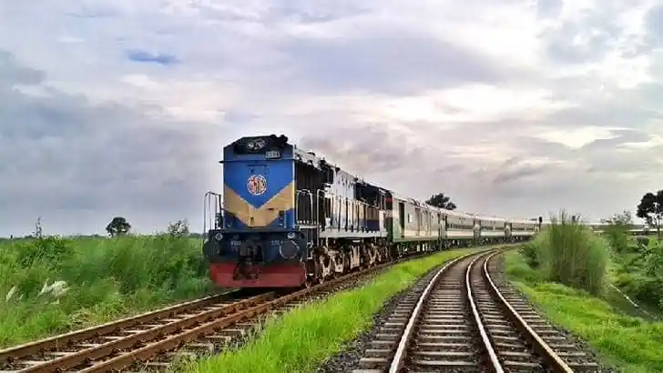 বাংলাদেশের রেলপথে একটি ট্রেন চলন্ত অবস্থায়, আকাশে মেঘাচ্ছন্ন আকাশ।. Channel i News - চ্যানেল আই নিউজ