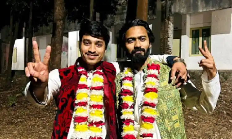 দুই ব্যক্তি ফুলের মালা পরা ও হাত উঁচু করে শুভেচ্ছা জানাচ্ছেন. Channel i News - চ্যানেল আই নিউজ