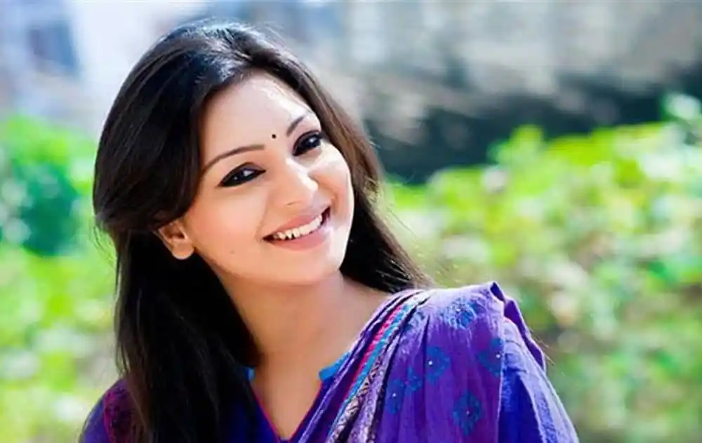 প্রভা হাসিমুখে ক্যামেরার দিকে তাকিয়ে, প্রাকৃতিক পটভূমিতে. Channel i News - চ্যানেল আই নিউজ