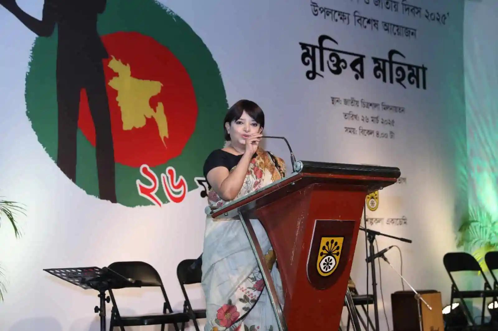 বাংলাদেশের নারী বক্তা ভাষণ দিচ্ছেন মঞ্চে, পেছনে সংগীত ও সাংস্কৃতিক অনুষ্ঠান. Channel i News - চ্যানেল আই নিউজ