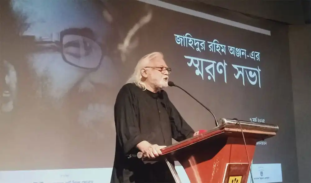 অঞ্জন দত্তের স্মরণ সভায় বক্তা, পেছনে তার ছবি ও নামের স্মরণিকা. Channel i News - চ্যানেল আই নিউজ