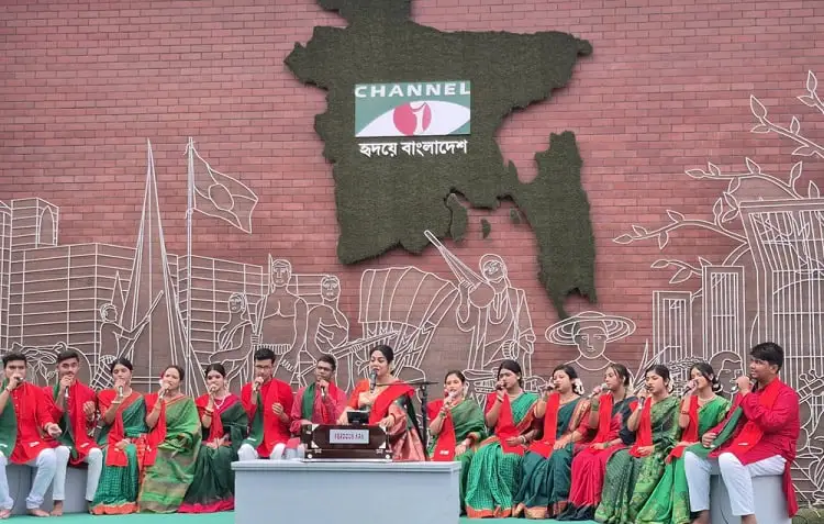 Channel i Bangladesh logo on a wall with women in traditional attire. Channel i News - চ্যানেল আই নিউজ
