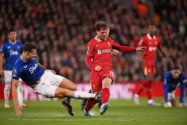 Liverpool footballer in red kit tackles opponent in blue kit during match. Channel i News - চ্যানেল আই নিউজ
