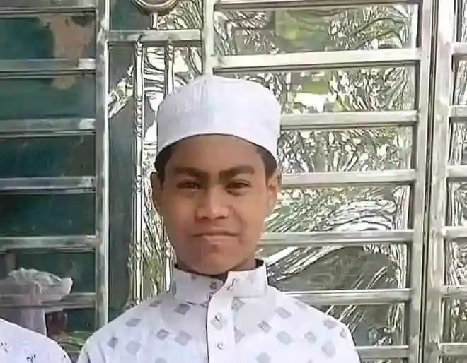Young boy wearing traditional white attire and cap, smiling at camera. Channel i News - চ্যানেল আই নিউজ