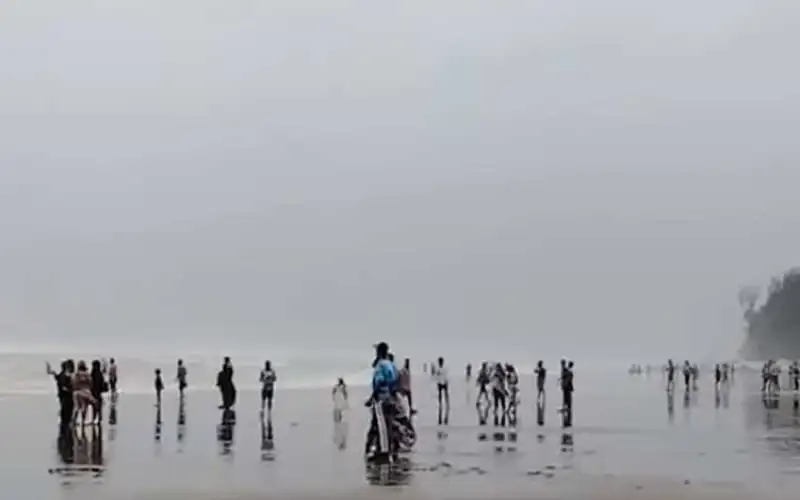 বালুচর সৈকত ও সমুদ্রের ধূসর আকাশের নিচে পর্যটকরা ঘুরে বেড়াচ্ছেন. Channel i News - চ্যানেল আই নিউজ