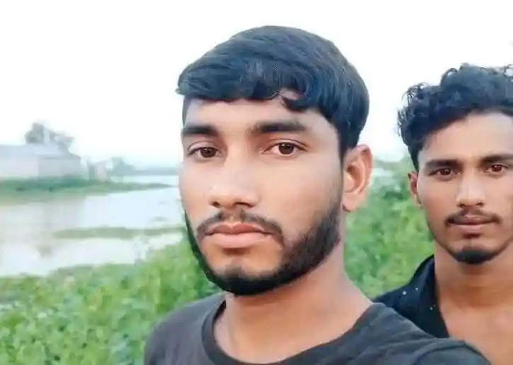 দুটি যুবক কৃষি জমির পাশে দাঁড়িয়ে ছবি তুলছেন।. Channel i News - চ্যানেল আই নিউজ