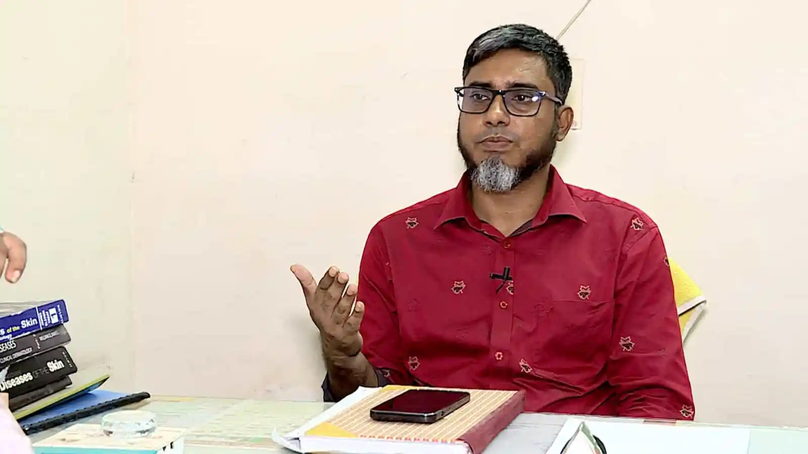 Bangladeshi man in red shirt speaking during interview or discussion. Channel i News - চ্যানেল আই নিউজ