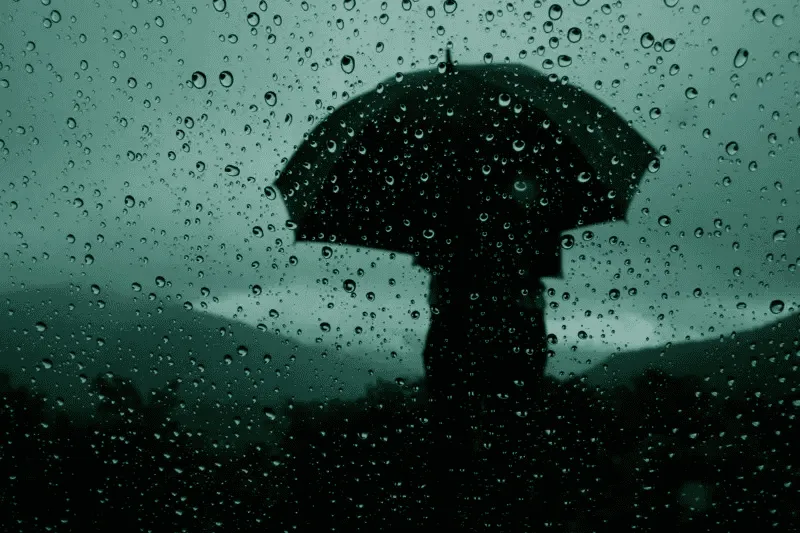Rainy weather with a person holding an umbrella in the rain. Channel i News - চ্যানেল আই নিউজ