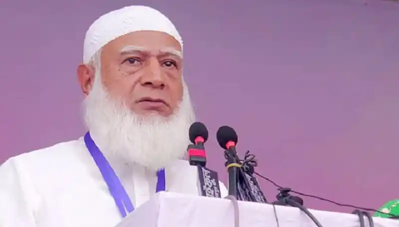 বাংলাদেশের একজন ধর্মীয় নেতা বক্তৃতা দিচ্ছেন, পেছনে মাইক্রোফোন ও পত্রিকা।. Channel i News - চ্যানেল আই নিউজ
