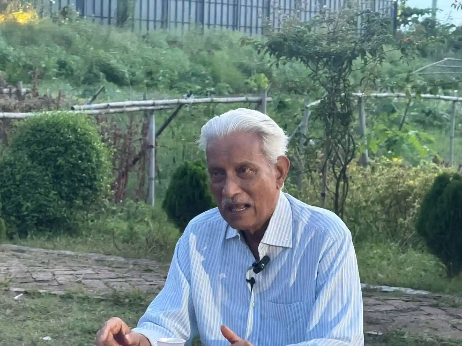 বৃদ্ধ ব্যক্তি outdoors, সবুজ গাছপালা ও ঝোপঝাড়ের মাঝে কথা বলছেন. Channel i News - চ্যানেল আই নিউজ