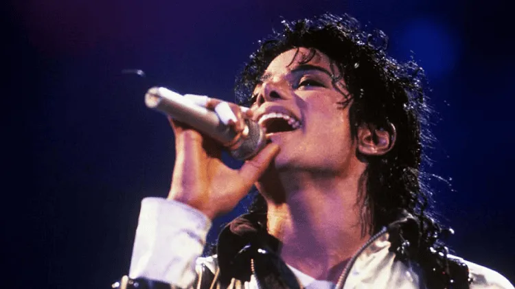 Michael Jackson performing on stage with a microphone, energetic expression. Channel i News - চ্যানেল আই নিউজ