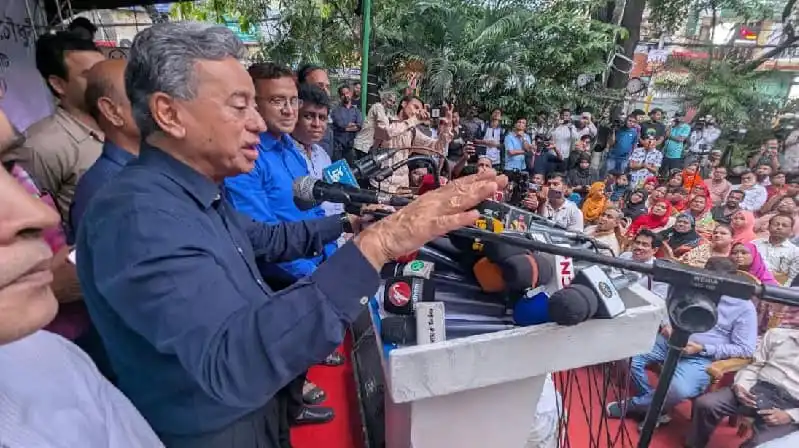 Amir Khasru addresses a crowd from a podium with microphones. Channel i News - চ্যানেল আই নিউজ