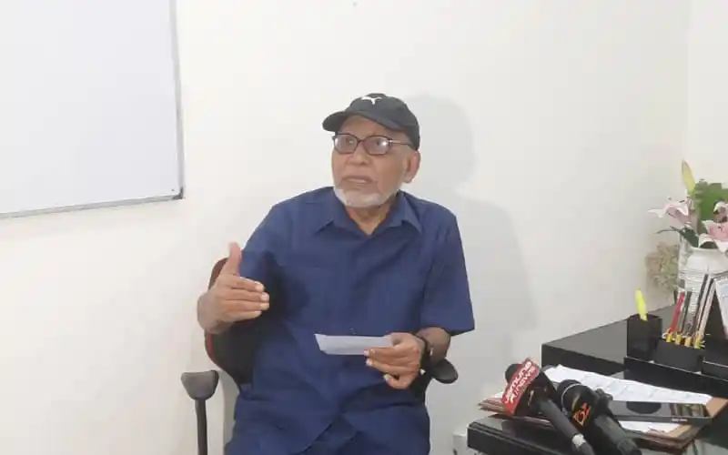 বক্তব্য দিচ্ছেন একজন পুরুষ শিক্ষক বা বক্তা, পেছনে সাদা বোর্ড ও ডেস্কে বিভিন্ন সামগ্রী।. Channel i News - চ্যানেল আই নিউজ
