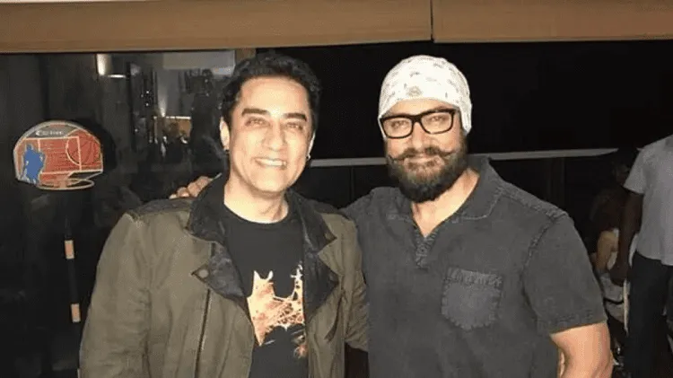 Two men smiling at an indoor event, one wearing a cap and glasses. Channel i News - চ্যানেল আই নিউজ