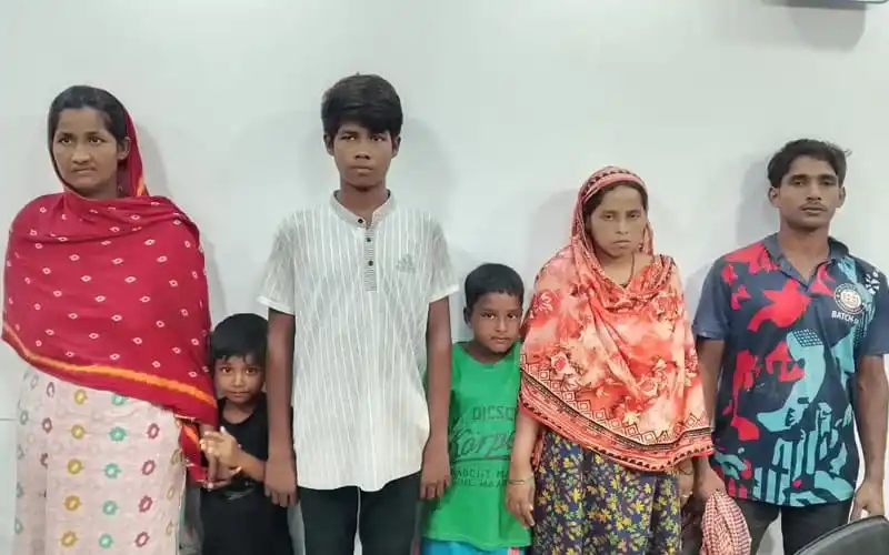 Six people, including women and children, standing indoors against a white wall. Channel i News - চ্যানেল আই নিউজ
