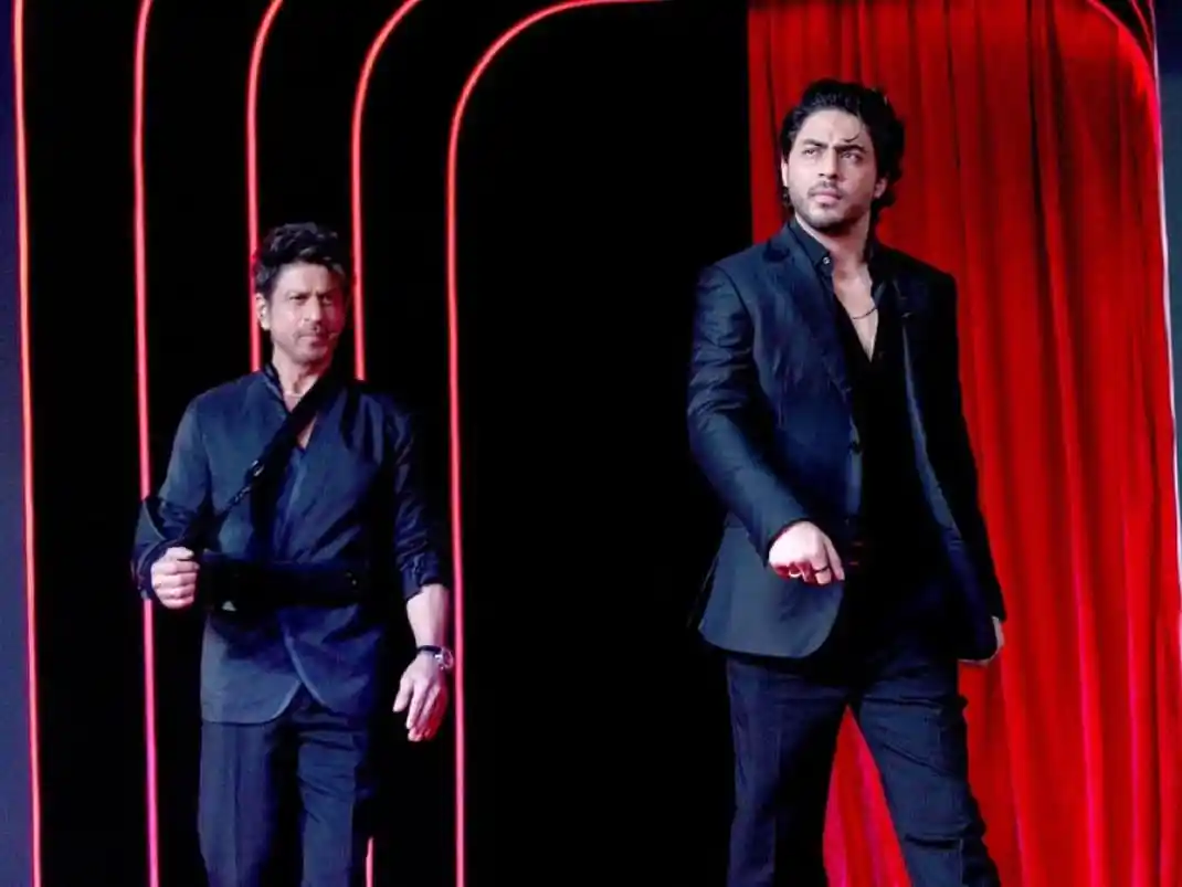 Two men in black suits on stage with red curtains behind them. Channel i News - চ্যানেল আই নিউজ