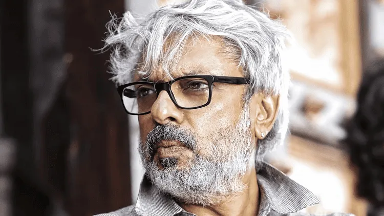 বয়সে প্রবীণ ব্যক্তি, চশমা পরা, হালকা রঙের চুল ও দাড়ি, পটভূমিতে ধূসর ও বাদামী রঙের পরিবেশ. Channel i News - চ্যানেল আই নিউজ