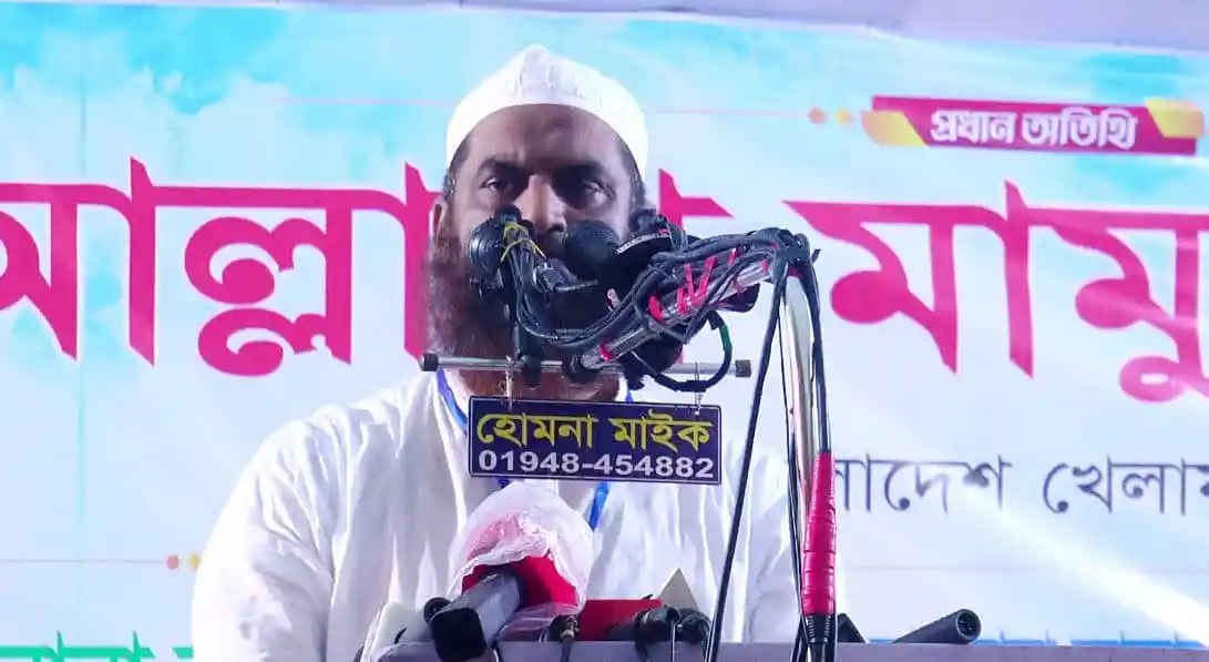 মামুনুল হক জনসম্মুখে ভাষণ দিচ্ছেন, পেছনে বাংলা লেখা ব্যানার. Channel i News - চ্যানেল আই নিউজ