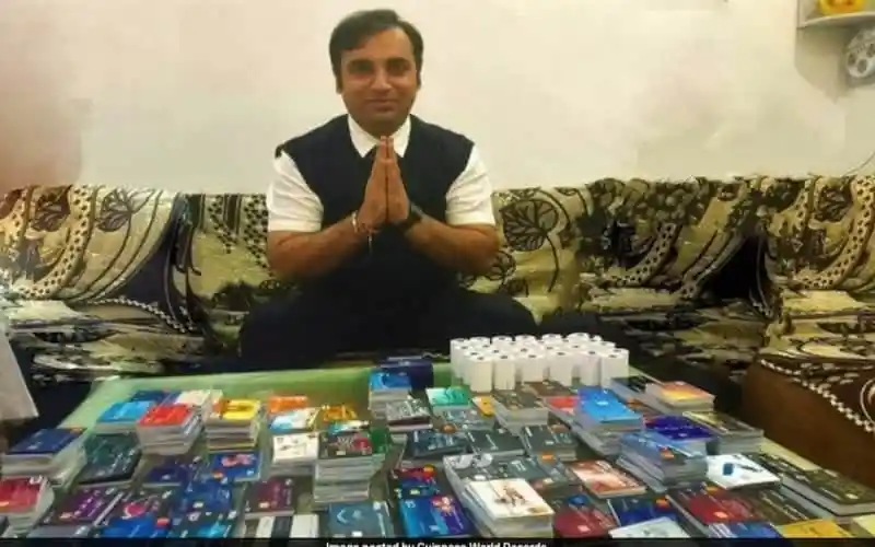 ব্যক্তি হাতে প্রণাম করে বসে, পাশে বিভিন্ন ক্রেডিট কার্ড ও গিনেস রেকর্ডের উপকরণ।. Channel i News - চ্যানেল আই নিউজ