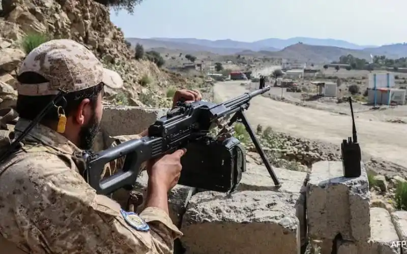 A soldier aiming a sniper rifle from a rocky outcrop in a mountainous area. Channel i News - চ্যানেল আই নিউজ